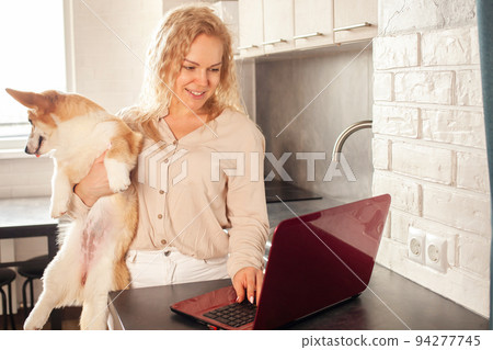 woman uses red laptop, works from home, freelances, watches movie with corgi dogs. Online shopping, communication, commerce. kitchen woman uses red laptop, works from home, freelances, watches movie with corgi dogs. Online shopping, communication, commerce. kitchen 94277745