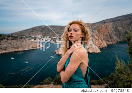 A woman in an emerald dress, a fashion model with long silk wings in a flowing dress, flying fabric on the embankment. 94278248