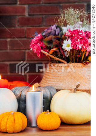 Festive composition for autumn holidays. Burning candle, various pumpkins and flowers bouquet in the wicker basket on brik wall background. Thanksgiving or Halloween. Fall Harvesting. Selective focus 94278540
