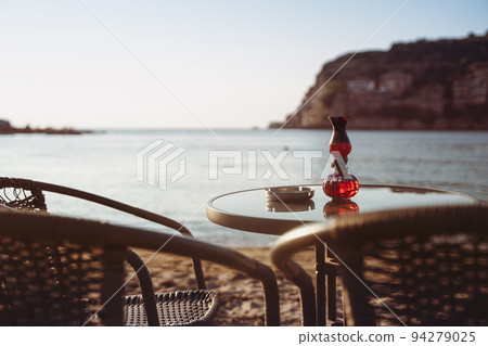 empty cafe table and chairs on sandy beach with ashtray and candle light in front of sea golf with clear sky before sunset 94279025