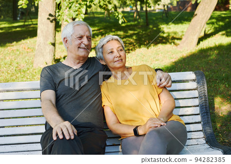 Elderly couple resting sit on bench in summer park Elderly couple resting sit on bench in summer park 94282385