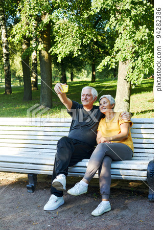 Older spouses make selfie picture or video call sit on bench in summer park 94282386