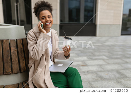 young african american woman sitting near the business center during lunch break with a laptop and a young african american woman sitting near the business center during lunch break with a laptop and a 94282930