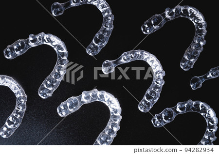 a pattern of invisible plastic aligners lie on a black background a pattern of invisible plastic aligners lie on a black background 94282934