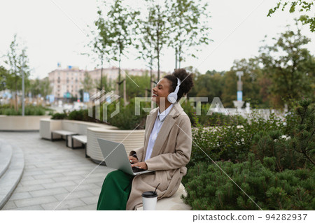 a young black student with a laptop sitting on a bench listening to music in headphones with a young black student with a laptop sitting on a bench listening to music in headphones with 94282937