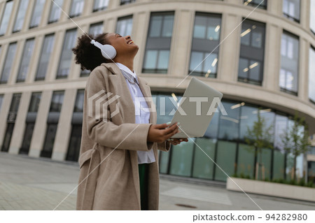 satisfied african american woman with a laptop in her hands and headphones emotionality laughs satisfied african american woman with a laptop in her hands and headphones emotionality laughs 94282980