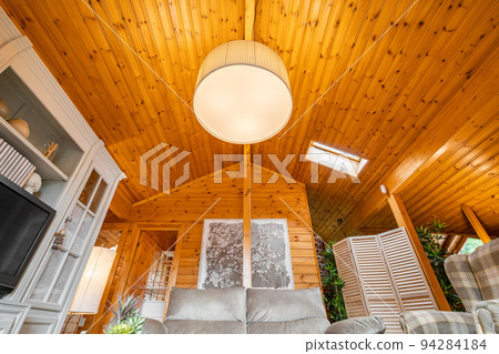 Bright living room with furniture, big lamp and sloping ceiling in a wooden cottage. Bright living room with furniture, big lamp and sloping ceiling in a wooden cottage. 94284184