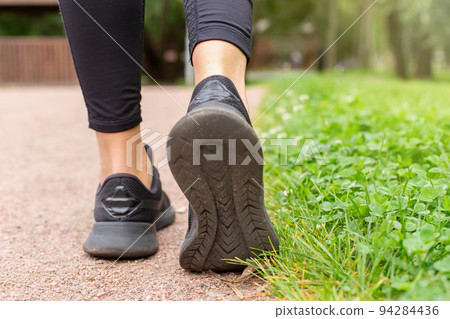 a womans legs, in black sneakers , walking along a path made of small red stone 94284436