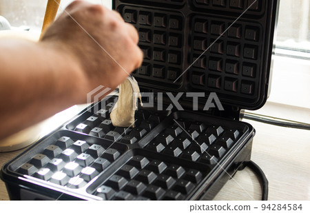 cooking Belgian waffles in a waffle iron. Pour in the dough. 94284584