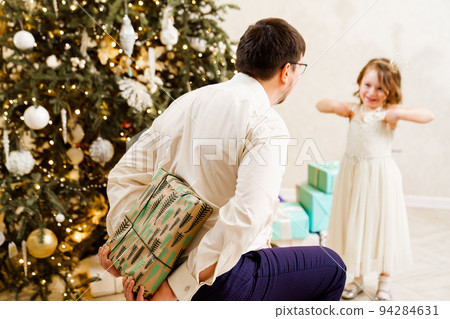 Dad hides behind his back a box with a gift for the baby daughter. Dad hides behind his back a box with a gift for the baby daughter. 94284631