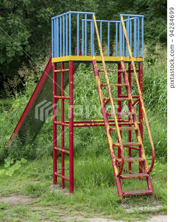 Deserted playground equipment in a park where plants grow 94284699