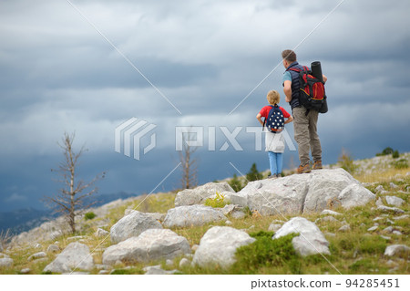 Cute schoolchild and mature father hiking together on mountain and exploring nature. Child learning survival skills and orienteering. Concepts of adventure, scouting and hiking tourism for kids. 94285451