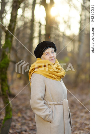 Portrait of beautiful senior woman during walk in autumn park. Old woman lady is walking outdoor. Activity and communication with nature is the secret of longevity. Portrait of beautiful senior woman during walk in autumn park. Old woman lady is walking outdoor. Activity and communication with nature is the secret of longevity. 94285585