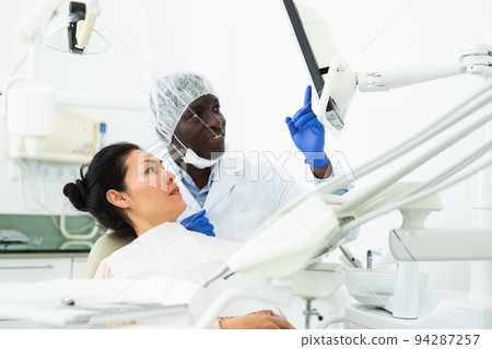Doctor dentist showing woman patient x-ray of teeth on computer 94287257