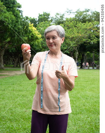 Portrait of happy senior adult elderly asia woman smiling standing with measuring tape and holding apple in the park. Portrait of happy senior adult elderly asia woman smiling standing with measuring tape and holding apple in the park. 94288486
