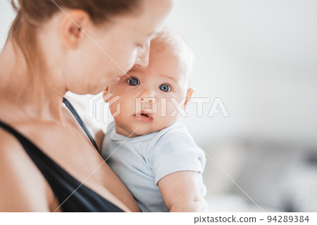 Portrait of sweet baby resting in mothers arms, looking at camera. New mom holding and cuddling little kid, embracing child with tenderness, love, care. Motherhood concept 94289384