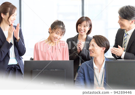 A young employee with an embarrassed smile and a mid-career or veteran employee praising her 94289446