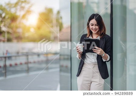 Young Asian businesswoman talking on phone and sitting in airport before business trip. Beautiful woman passenger has mobile call and discusses something with smile, holds coffee in hand 94289889