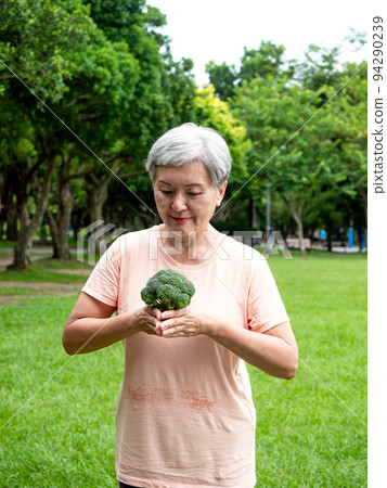 快樂的樂齡亞洲婦女微笑著站著,手上拿著有機蔬果,享受公園裡的大自然新鮮空氣,適用於老人健康飲食或素食 94290239
