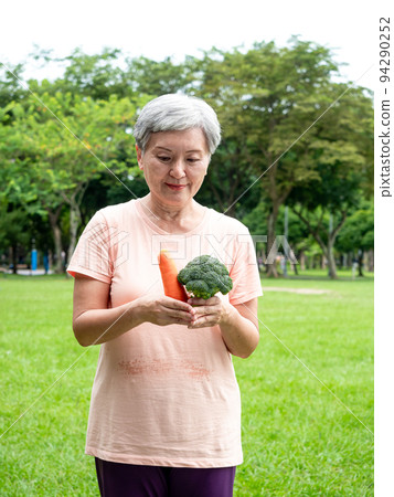 Happy senior asian woman smiling and standing with organic fruits and vegetables in hands enjoying nature fresh air in park, suitable for elderly healthy eating or vegetarian food Happy senior asian woman smiling and standing with organic fruits and vegetables in hands enjoying nature fresh air in park, suitable for elderly healthy eating or vegetarian food 94290252