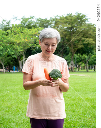 快樂的樂齡亞洲婦女微笑著站著,手上拿著有機蔬果,享受公園裡的大自然新鮮空氣,適用於老人健康飲食或素食 快樂的樂齡亞洲婦女微笑著站著,手上拿著有機蔬果,享受公園裡的大自然新鮮空氣,適用於老人健康飲食或素食 94290254