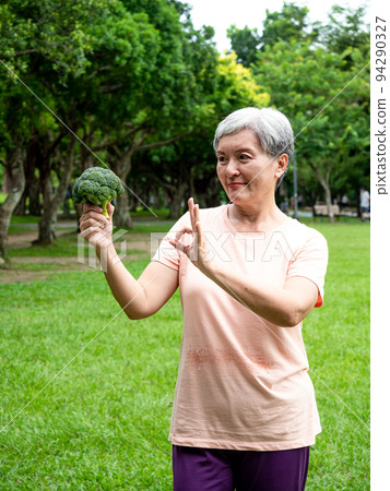 快樂的樂齡亞洲婦女微笑著站著,手上拿著有機蔬果,享受公園裡的大自然新鮮空氣,適用於老人健康飲食或素食 94290327