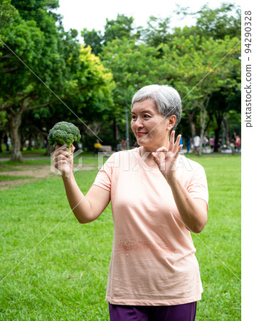 快樂的樂齡亞洲婦女微笑著站著,手上拿著有機蔬果,享受公園裡的大自然新鮮空氣,適用於老人健康飲食或素食 94290328