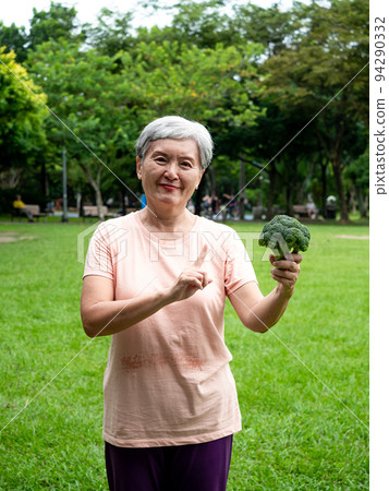 快樂的樂齡亞洲婦女微笑著站著,手上拿著有機蔬果,享受公園裡的大自然新鮮空氣,適用於老人健康飲食或素食 94290332