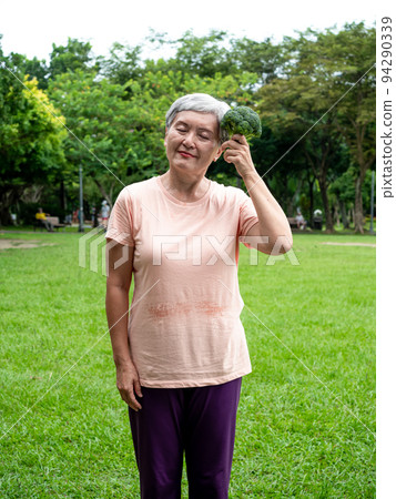 Happy senior asian woman smiling and standing with organic fruits and vegetables in hands enjoying nature fresh air in park, suitable for elderly healthy eating or vegetarian food Happy senior asian woman smiling and standing with organic fruits and vegetables in hands enjoying nature fresh air in park, suitable for elderly healthy eating or vegetarian food 94290339