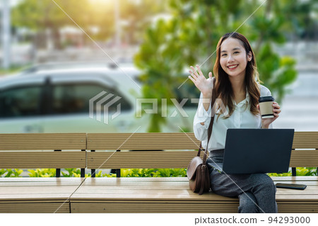 Smiling Asian curly business woman wearing trendy sitting in the central city street and uses her phone and laptop. Pretty summer woman in white shirt walks down the street looking at her mobile phone Smiling Asian curly business woman wearing trendy sitting in the central city street and uses her phone and laptop. Pretty summer woman in white shirt walks down the street looking at her mobile phone 94293000
