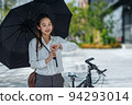 Cute Asian business woman with holding black umbrella looking at watch outdoors on sunny day 94293014