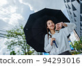 Cute Asian business woman with holding black umbrella looking at watch outdoors on sunny day, focus to the watch 94293016