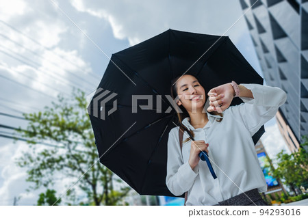 Cute Asian business woman with holding black umbrella looking at watch outdoors on sunny day, focus to the watch Cute Asian business woman with holding black umbrella looking at watch outdoors on sunny day, focus to the watch 94293016