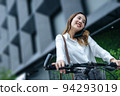 Young Asian businesswoman wearing helmet and standing on a city street with bicycle looking at phone. 94293019