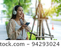 Beautiful Asian woman listening favourite music on headphones from mobile phone, Happiness relaxation summer in park with music riding bicycle in green park. 94293024