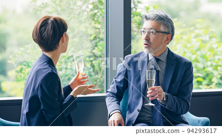 Executive man and woman chatting while drinking champagne in the lobby 94293617