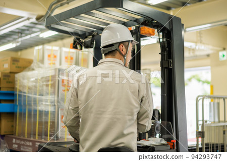 Qualified male employee driving forklift in distribution warehouse Qualified male employee driving forklift in distribution warehouse 94293747