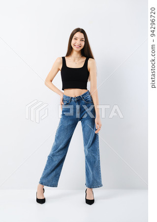Portrait of laughing young woman in black tank top and wide jeans 94296720