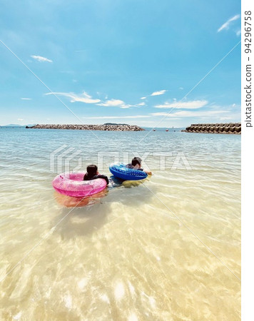 Parents and children swimming side by side with floating rings in the sea Parents and children swimming side by side with floating rings in the sea 94296758