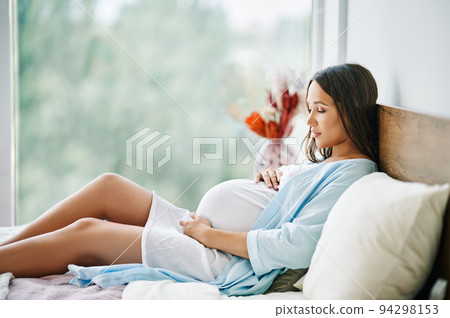 Portrait of happy pregnant woman lying in bed and touching her belly at home Portrait of happy pregnant woman lying in bed and touching her belly at home 94298153
