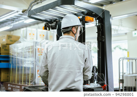 Qualified male employee driving forklift in distribution warehouse Qualified male employee driving forklift in distribution warehouse 94298801