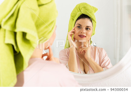 Woman with towel on his head near mirror and touching face 94300034