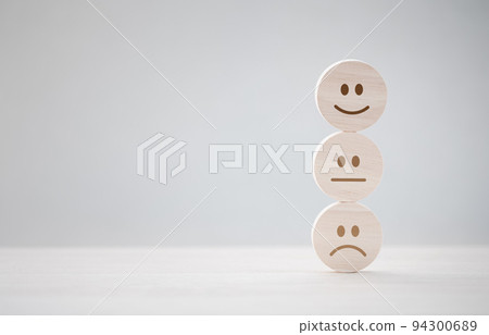 closeup happy emotion face on wooden piece with unhappy one behind for satisfaction survey 94300689