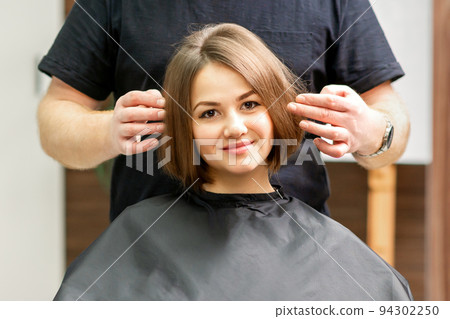 Gorgeous brunette short hair woman and her male hairdresser looking and checking out hairstyle. Beautiful hairstyle of a young brunette woman, results of hair treatment in a beauty salon 94302250