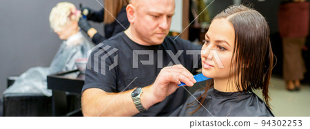 Haircut of long wet hair of young caucasian woman by a male hairdresser in a hairdresser salon Haircut of long wet hair of young caucasian woman by a male hairdresser in a hairdresser salon 94302253