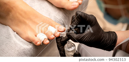 Manicure master painting nails on a female foot with transparent nail polish in a beauty salon, close up Manicure master painting nails on a female foot with transparent nail polish in a beauty salon, close up 94302313