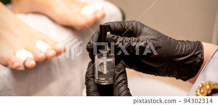 Transparent nail polish in the hands of a manicure master while painting nails on a female feet Transparent nail polish in the hands of a manicure master while painting nails on a female feet 94302314