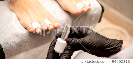 White nail polish in the hands of a manicurist while painting nails on a female feet, closeup 94302316