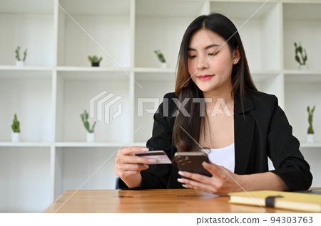 Asian businesswoman holding a credit card and a smartphone, using mobile banking. Asian businesswoman holding a credit card and a smartphone, using mobile banking. 94303763