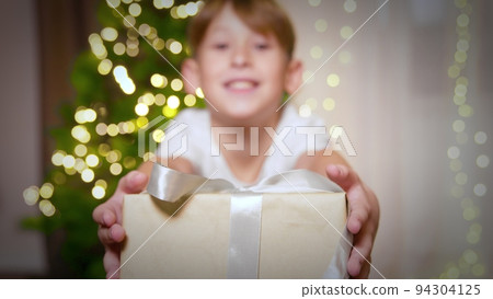 A boy at Christmas waves his hand at the camera and gives a gift 94304125